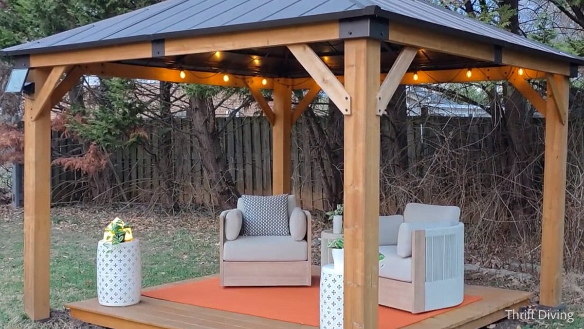 How to Make DIY Gazebo Screens - Backyard wooden gazebo with lighting and white furniture and orange rug.