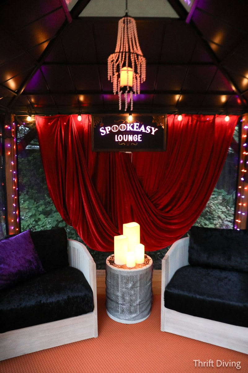 Red velvet backdrop with SpookEasy sign in cozy outdoor Halloween decorations in gazebo.