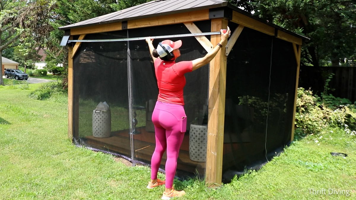 Measuring a screened gazebo with a tape measure.